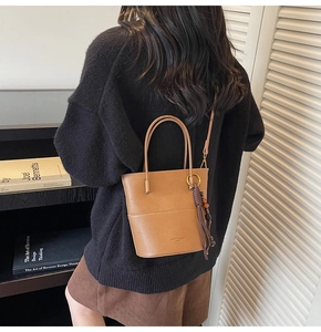 Brown leather bucket bag with fringe tassel shown worn crossbody by a model in a cozy setting