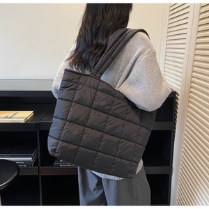 Detail of a large black quilted tote bag with square stitching shown on model shoulder