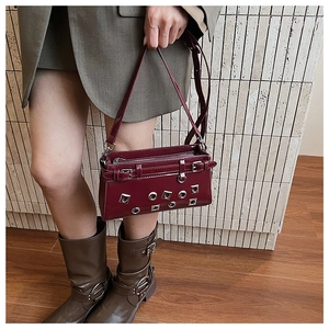 Detail view of burgundy crossbody bag with silver studs and buckles worn by model