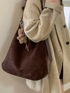 Brown vintage hobo tote bag in suede with a plush bear charm on a model in a beige coat