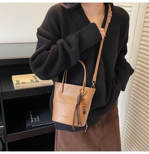 Brown vintage bucket bag with tassel detail worn by a model in a cozy library setting
