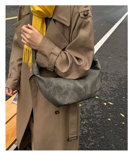Detail of dark hobo bag with white stitching and wide shoulder strap on beige coat
