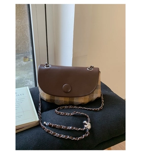 Detail of retro saddle bag featuring brown leather flap and classic plaid fabric texture