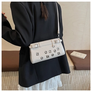 Detail of cream white patent leather crossbody bag with silver eyelets on a black blazer