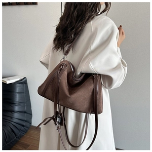 Detail of dark brown suede tote bag featuring metallic lock pendant and long strap
