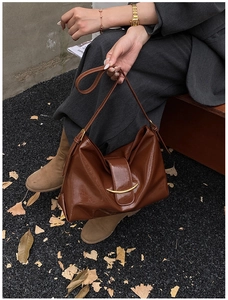 Détail d'un sac cabas en cuir verni plissé marron foncé avec barre dorée courbée
