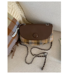 Detail of saddle bag with brown leather flap, plaid wool fabric, and chain strap