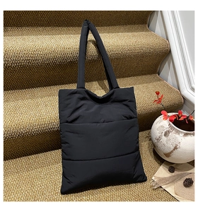 Close-up of black quilted puffer tote bag with padded straps on a stylish indoor staircase