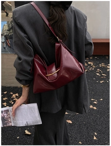 Détail du sac cabas en cuir verni bordeaux avec garniture dorée porté à l'épaule