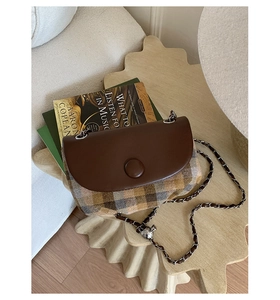 Detail of vintage plaid saddle bag with leather flap and woven chain strap on a table