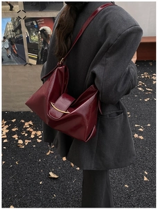 Détail du sac cabas en cuir verni bordeaux avec boucle dorée porté par un mannequin femme