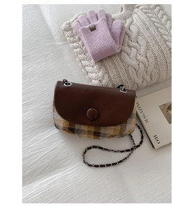Flat lay of retro plaid saddle bag with chain strap on a white striped bed sheet