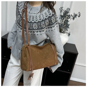 Detail of brown suede tote bag with leather trim and lock charm worn on shoulder