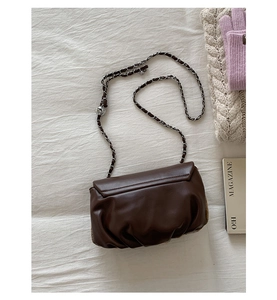 Detail of soft brown pleated cloud bag with silver chain and metal bead on white fabric