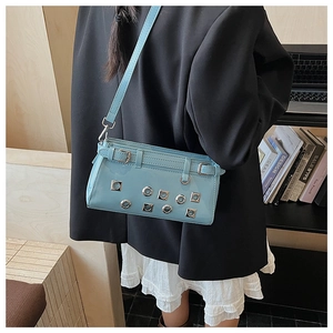 Detail of light blue patent leather crossbody bag with silver eyelets shown on a model