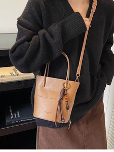 Brown leather bucket bag with textured finish, featuring unique tassel beads and gold accents