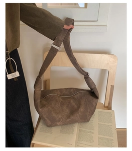 Detailed view of brown suede crescent bag with wide adjustable strap on a chair