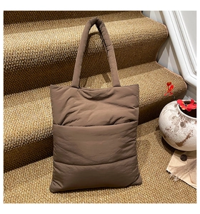 Detail of a brown quilted puffer tote bag with padded handles on a carpeted staircase