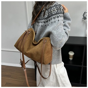 Detail of brown suede tote bag with metal handle and leather shoulder strap worn by model