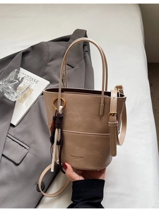 Khaki PU leather bucket bag with woven charm on a minimalist aesthetic background