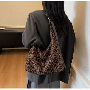 Model wearing a large leopard print hobo shoulder bag with leather strap in a home setting