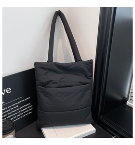 Close-up of black quilted puffer tote bag with padded strap on minimalist decor