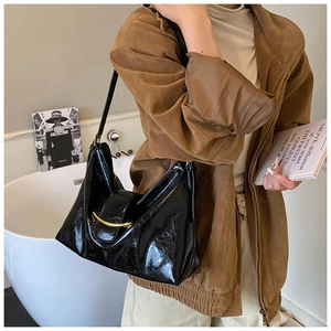 Détail du sac hobo noir brillant avec boucle croissant dorée et texture froissée douce