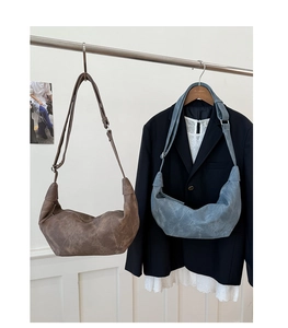 Detail of vintage half-moon crossbody bags in brown and blue suede on a hanger