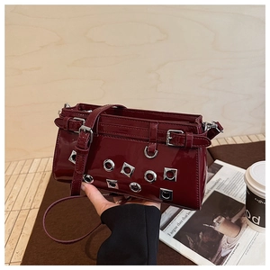 Detail of burgundy patent leather shoulder bag with silver eyelets and buckle strap