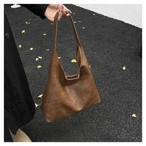 Brown vintage textured faux leather tote bag held by hand in outdoor autumn setting