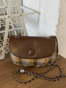 Retro saddle bag with plaid fabric and brown leather flap on a wooden tabletop