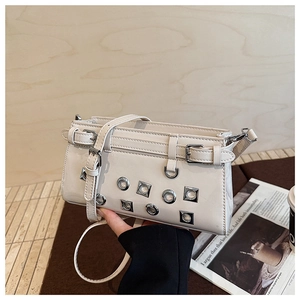 Detail of cream leather crossbody bag with punk style metal eyelets and adjustable strap