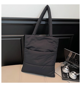 Detail of black quilted puffer tote bag showing padded texture and side zipper pocket