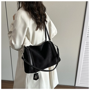 Detail view of the black suede tote bag showing the side leather trim and metal clasp