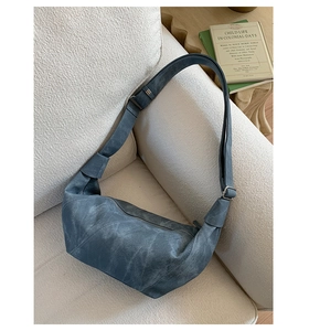 Detail view of retro blue hobo bag in distressed leather texture on a white sofa