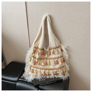Sac fourre-tout en maille bohème avec pompons et plumes blanches sur fond crème doux