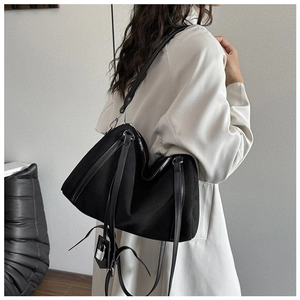 Detail of black suede tote bag with fringe straps and silver padlock charm on model