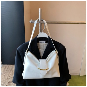 Détail d'un sac bandoulière en cuir verni blanc avec boucle dorée sur blazer noir
