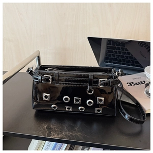 Detail of black patent leather crossbody bag with silver eyelets and buckle straps