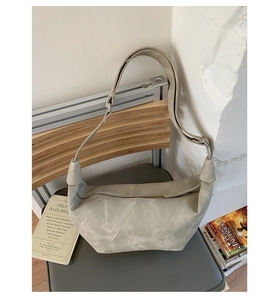 Detail of grey suede hobo bag with adjustable strap and stitching on a textured chair