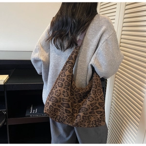 Detail of a large leopard print tote bag with brown leather straps shown on a model