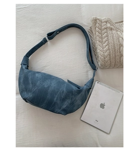 Detail view of a vintage blue crescent shoulder bag on fabric with a tablet and sweater