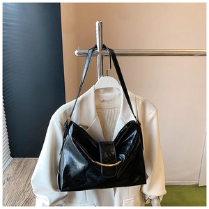 Détail du sac croissant noir brillant avec barre métallique dorée et texture plissée