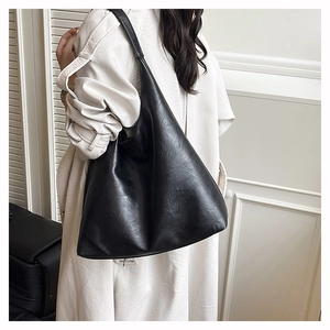Detailed view of large black tote bag with leather texture on trench coat shoulder