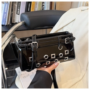 Detail of black patent leather bag featuring silver metal eyelets and adjustable straps