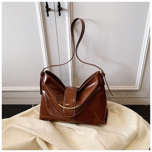 Détail d'un cabas en cuir verni marron avec barre métallique dorée et bandoulière réglable