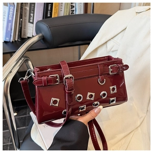 Detail of dark red patent leather crossbody bag with silver eyelet and rivet accents