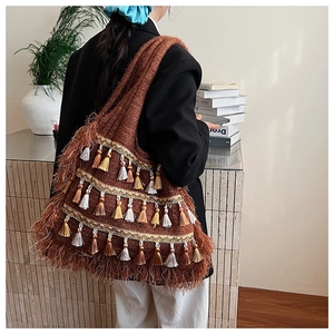 Détail du sac cabas bohème en tricot avec pompons colorés sur l'épaule d'un mannequin
