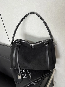 Modern black suede tote bag with leather trim and silver padlock charm in minimalist setting