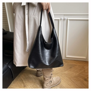 Minimalist black matte leather tote bag worn by a model in a cozy indoor setting